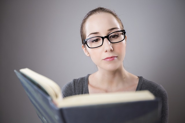 Femme aux cheveux attachés et avec des lunettes qui lit un livre